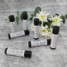 Load image into Gallery viewer, Truth Cosmetics vegan lip balm tubes in assorted flavors on a gray textured background with white flowers and greenery