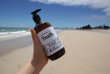 Load image into Gallery viewer, Truth Cosmetics vegan face wash in brown pump bottle held by hand on sunny sandy beach