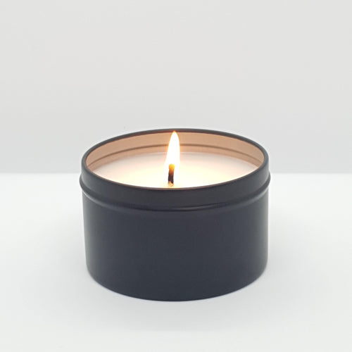 Australian bush vegan candle in matte black tin with single lit wick on white background
