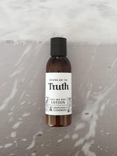 Load image into Gallery viewer, Truth Cosmetics vegan face and body lotion bottle with grapefruit and cedarwood scent on wet surface
